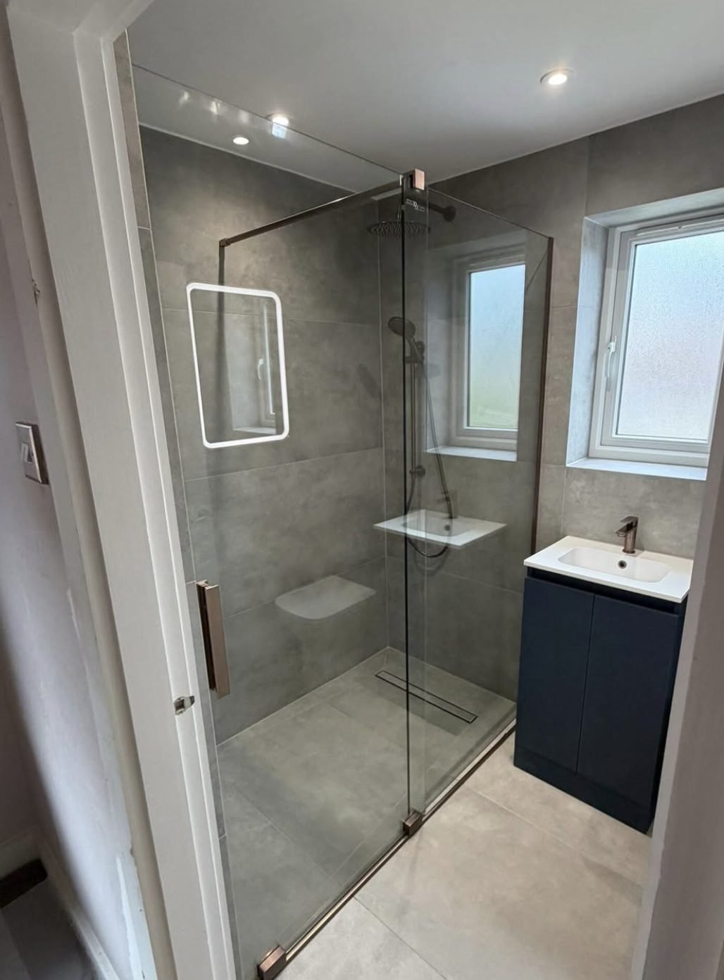 Walk in shower with a linear drain, glass screen and navy vanity unit